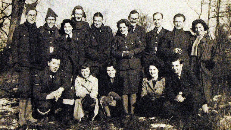 15 men and women in uniform standing and squatting in two rows in a black and white photograph
